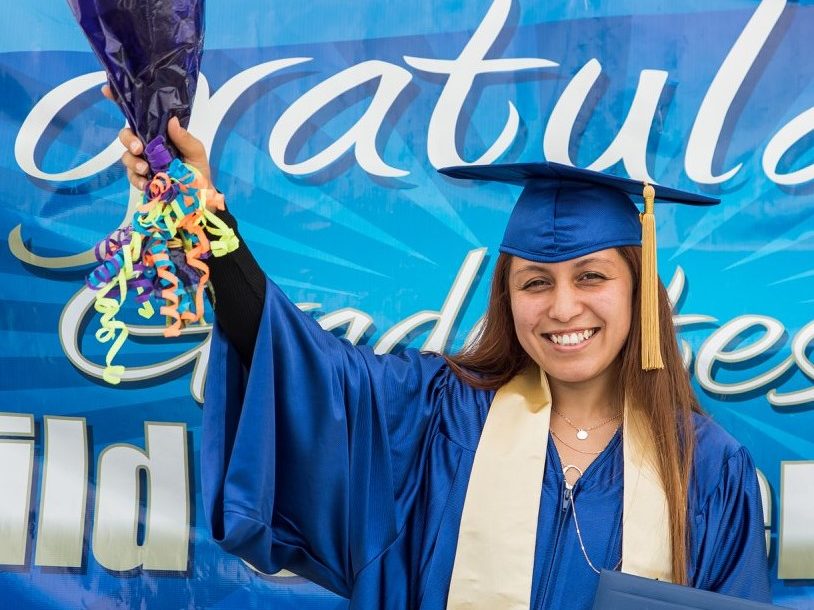Happy female teen graduate holding up flowers and diploma